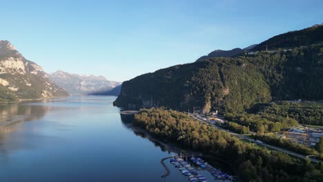 Fliegen-Sie-über-Einen-Kleinen-Yachthafen,-In-Dem-Segelboote-Angedockt-Sind-Und-Das-Wasser-In-Blauen-Farbtönen-Schimmert,-Im-Walensee,-Schweiz