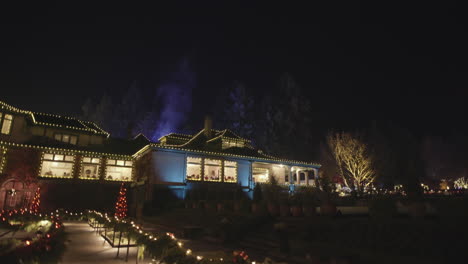 wide shot of house decorated with christmas lights and smoke coming from chimney, night