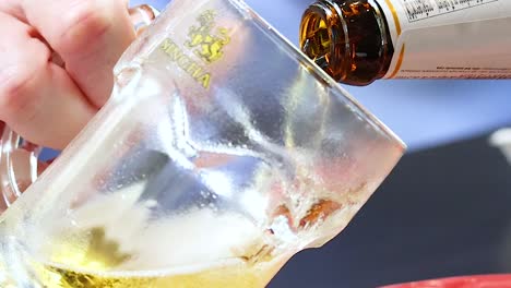 detailed view of golden beer being poured from a bottle into a glass mug, creating foam.
