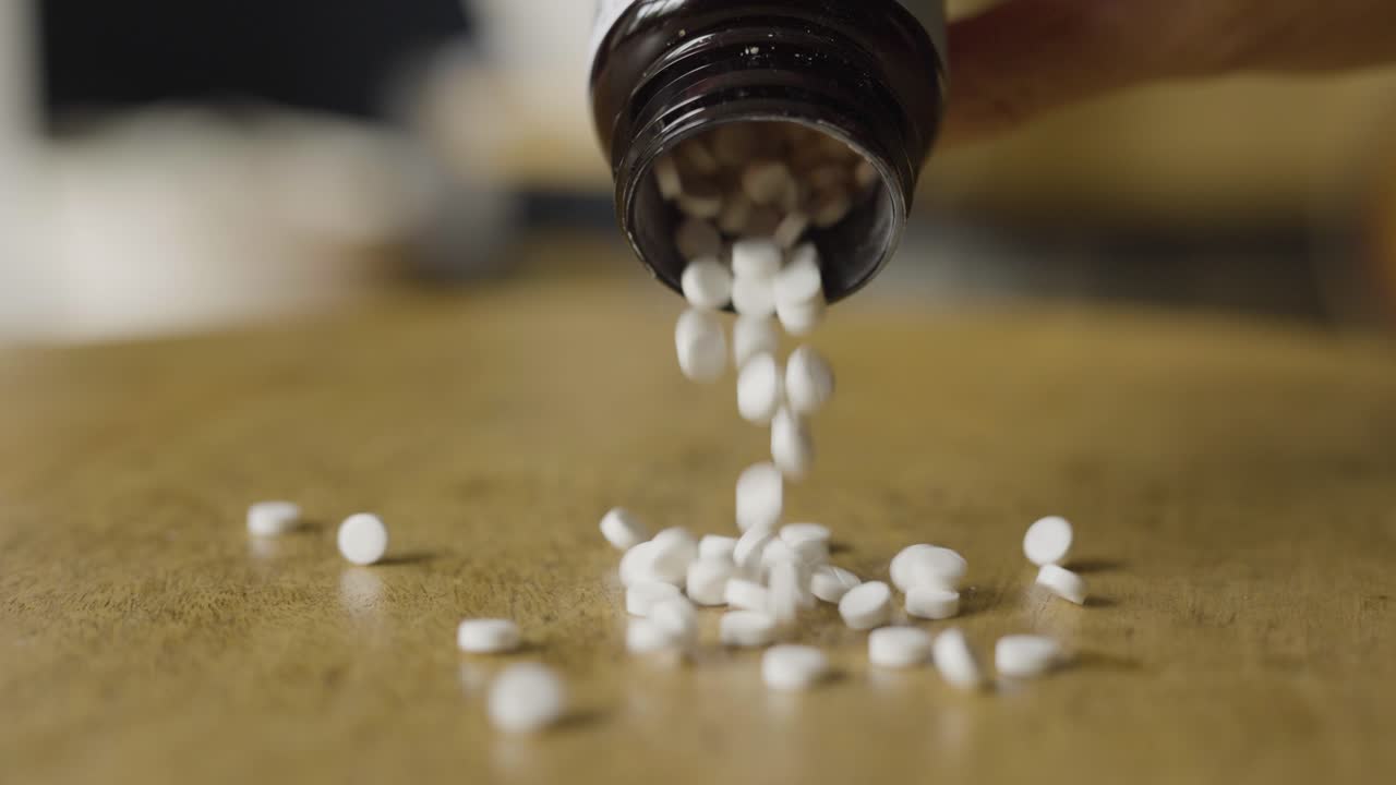 Primo piano al rallentatore di pillole bianche che cadono da una bottiglia, a simboleggiare farmaci e uso farmaceutico