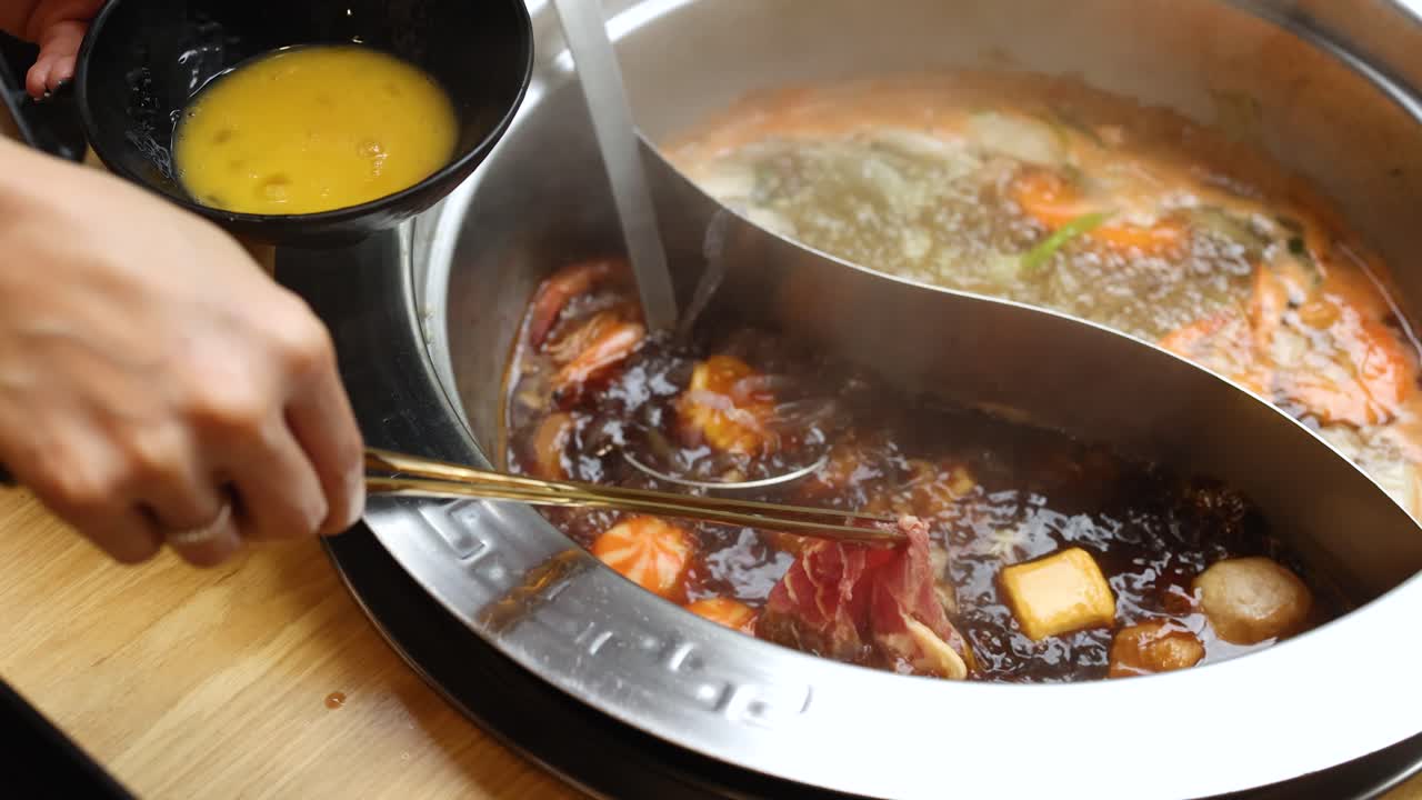 Hand dips raw beef in egg, cooks it in dual-broth hotpot at restaurant table