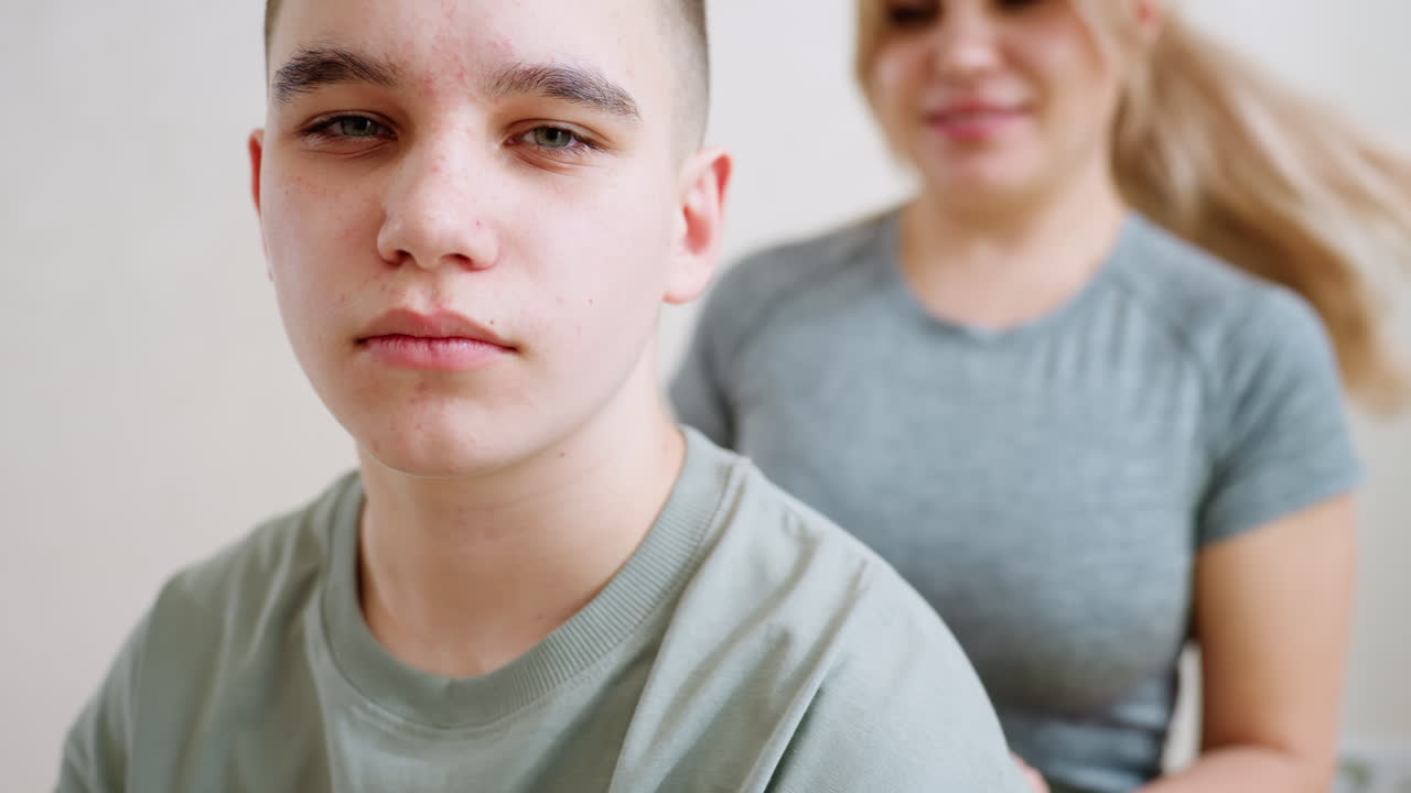 Woman sitting behind boy with hands on his shoulders indoors, showing care, guidance and support in quiet moment, highlighting family bond and mentorship