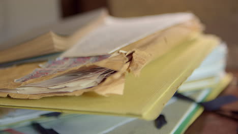 a man's hand places a yellow folder and an old torn envelope on a disorganized pile of folders