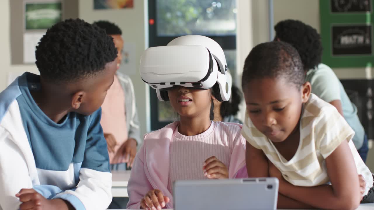 Afroamerikansk barn tager et hvidt VR-headset på ved skrivebordet efter en teknologitime, mens kammerater ser på en tablet.