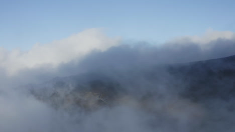 wispy clouds rise pushing across slopes of haleakala, aerial overview