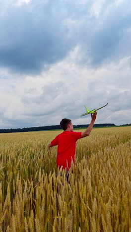 boy launching toy plane in the field. teenager runs with plane on yellow field under blue sky. happy child playing in summer nature. vertical video