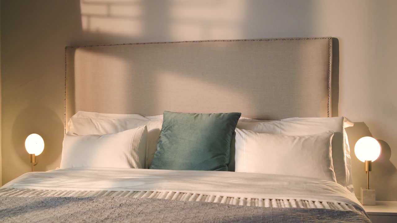 Camera is pulling back from bed to reveal pillow arrangement as sunlight is casting moving shadows
