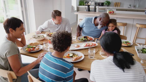 multi-generation mixed race family eating meal around table at home together