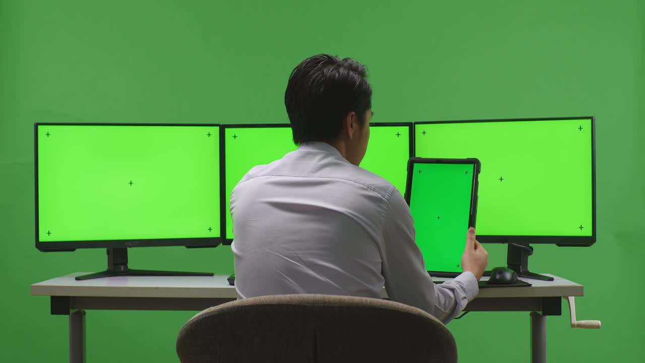 녹색 화면 환경에서 태블릿과 여러 모니터를 사용하는 사람