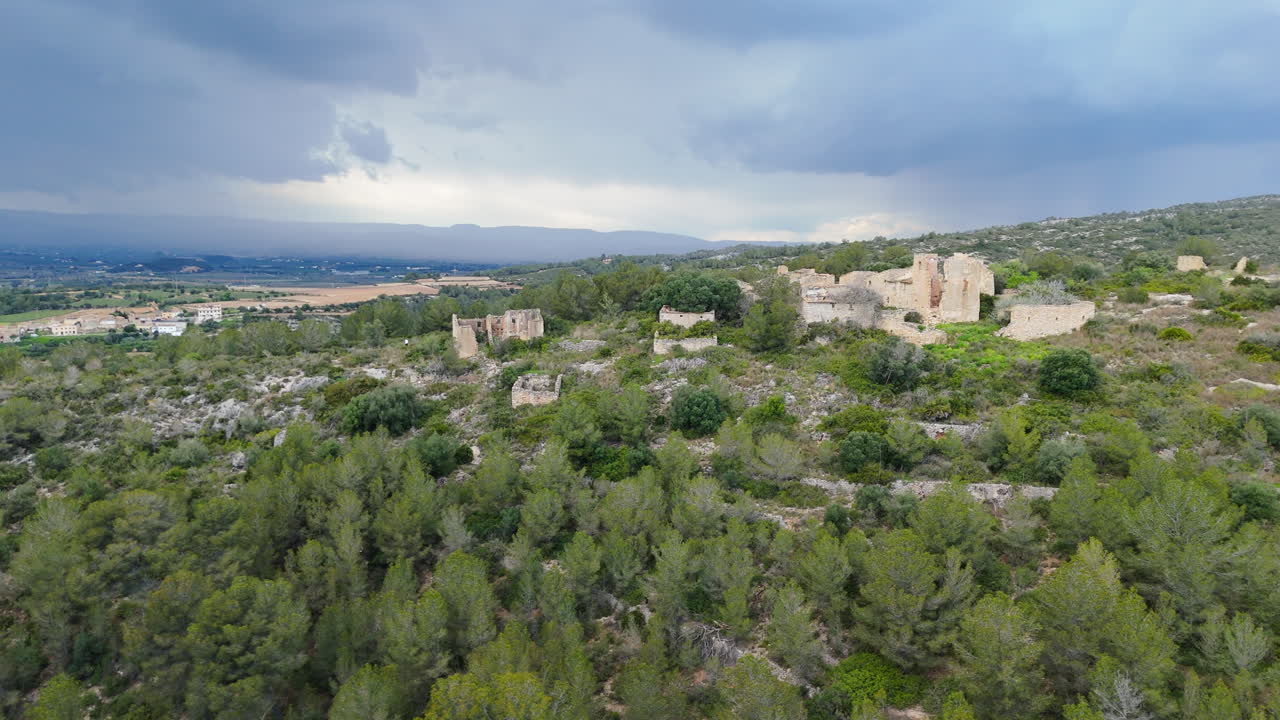 Vista aerea cinematografica realizzata con drone di antiche rovine in pietra circondate da colline alberate e un'ampia valle di campagna sotto un cielo nuvoloso spettacolare