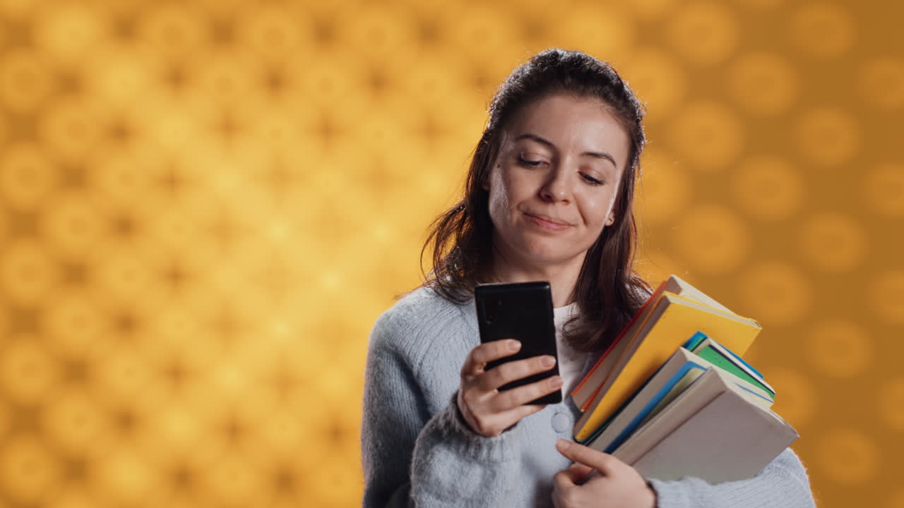 mujer sonriente leyendo mensajes en su teléfono inteligente mientras sostiene una pila de libros