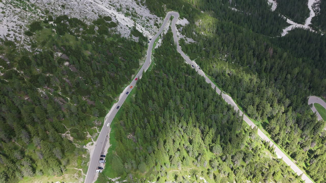 Aerial drone view of three luxury sports cars driving along a mountain slope road in the Alps, surrounded by forest and summer scenery