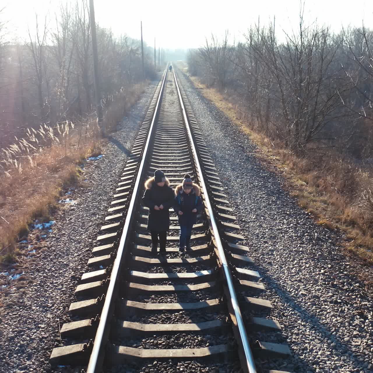 Two little boys walking on a railroad. Children in warm clothes go on a rail on nature background in winter time.