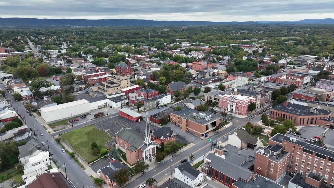 Aerial orbit wide shot of american town with historic building and church tower. Traffic scene on street on cloudy day in fall season. Martinsburg, Virginia, USA