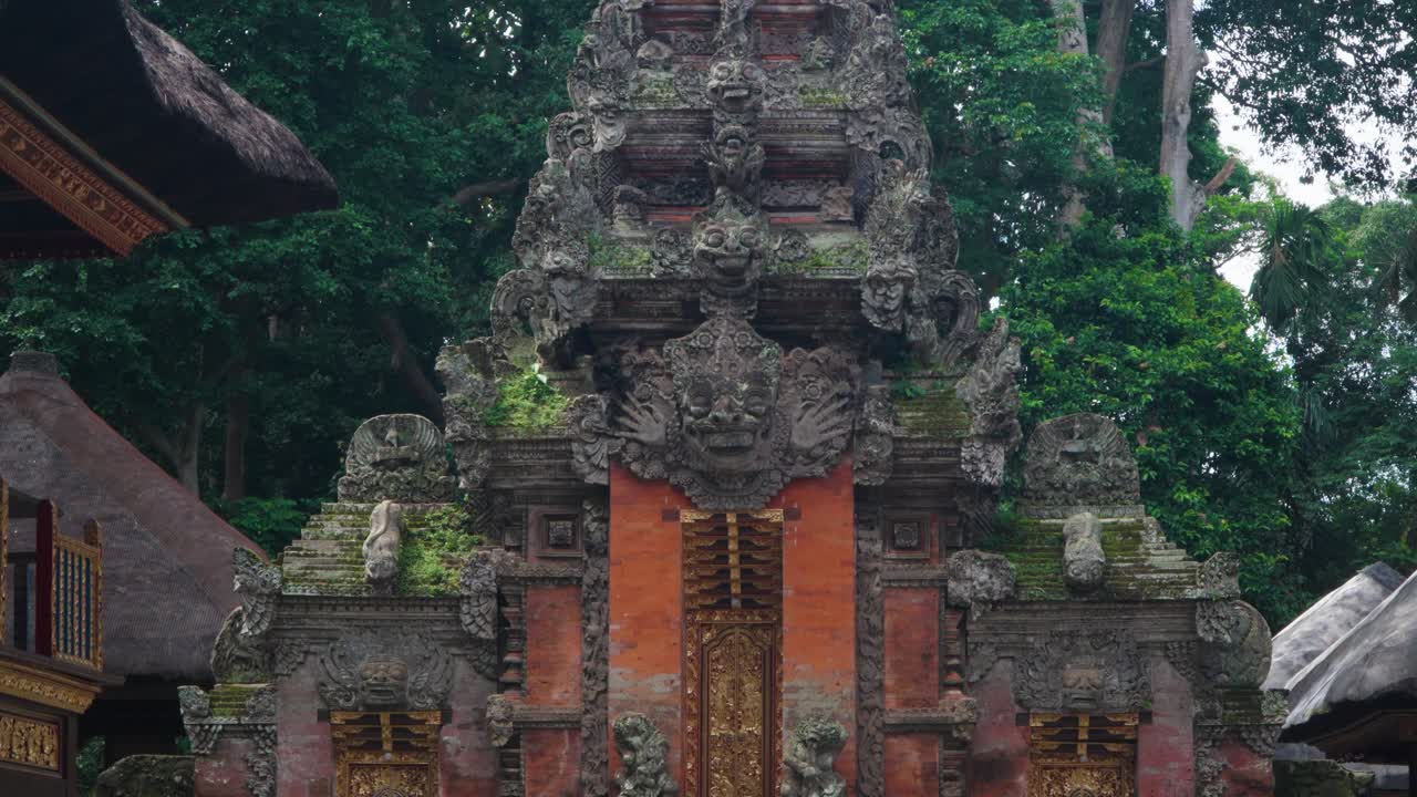 Ornate Balinese temple gateway in Ubud Monkey Forest, Bali, framed by ancient statues and vibrant jungle foliage, establishing tilt along golden doors with carved faces
