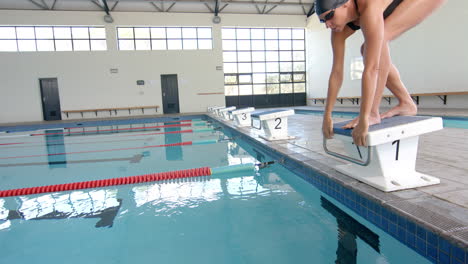 Swimmer-poised-on-starting-block-at-indoor-pool