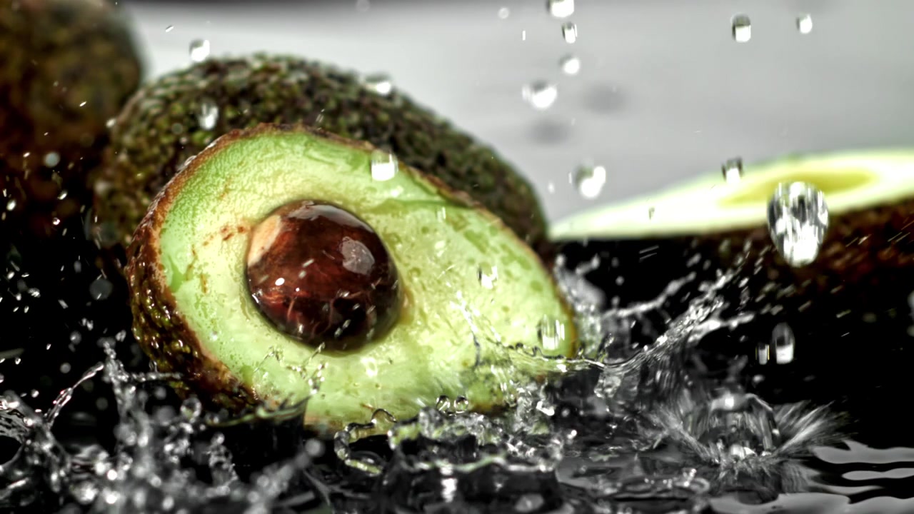Schizzi d'acqua al rallentatore su avocado fresco tagliato a metà