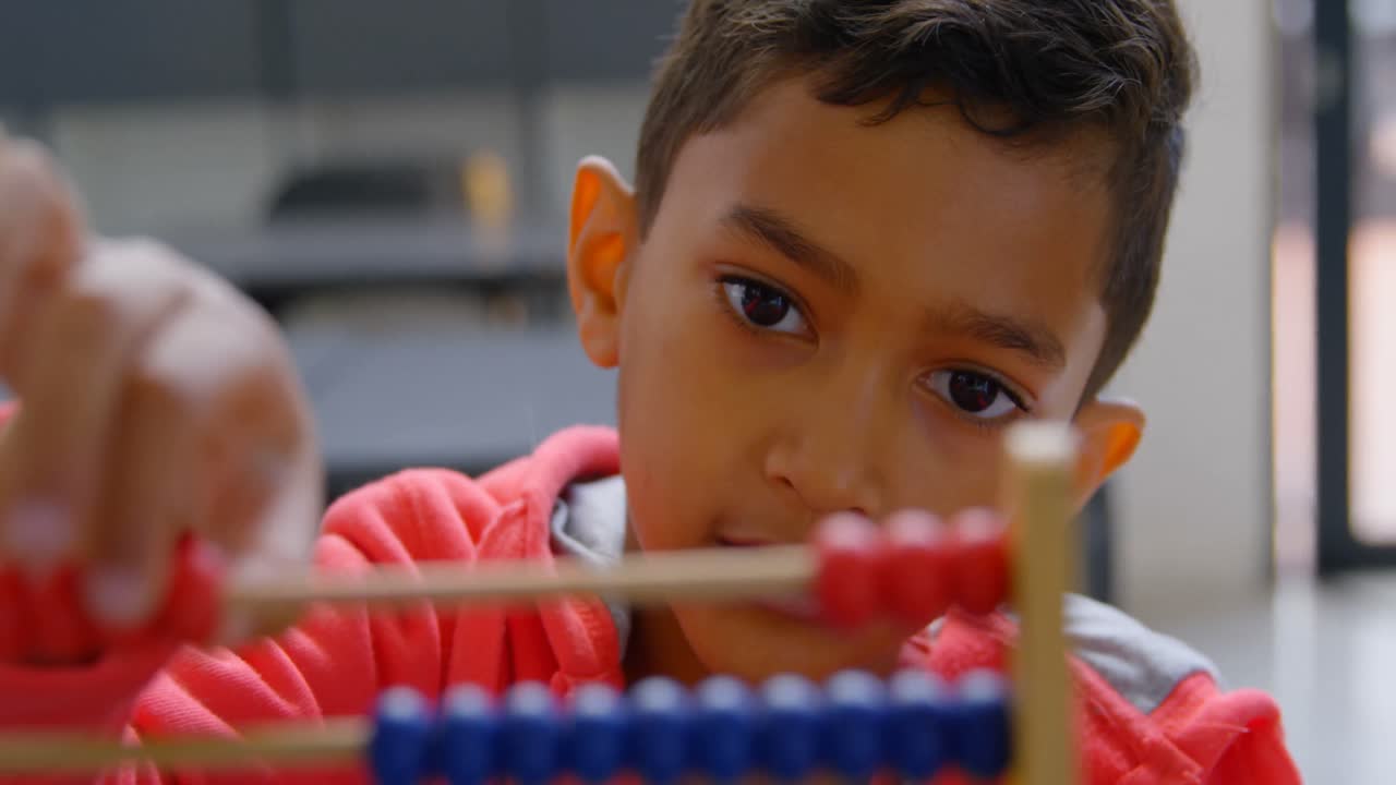 Front view of Asian schoolboy solving math problem with abacus at desk ...