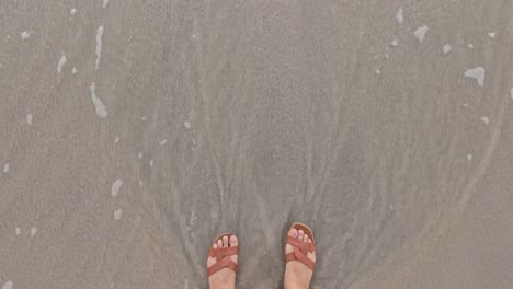 feet walking as waves wash over sandy beach