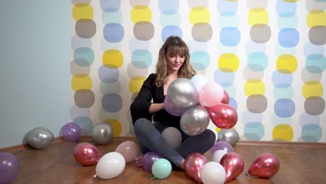 Junge-Frau-Sitzt-Um-Luftballons-Herum-Und-Spielt-Mit-Luftballons-Vor-Buntem-Hintergrund