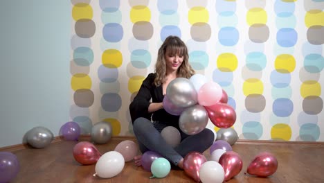 mujer joven sentada alrededor de globos y jugando con globos contra un fondo colorido