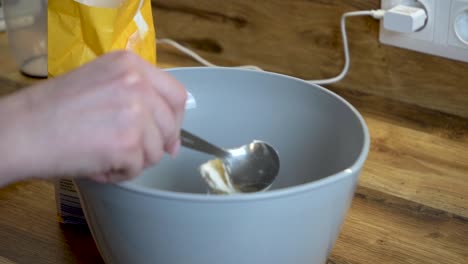 woman adding a spoon of flour to a bowl