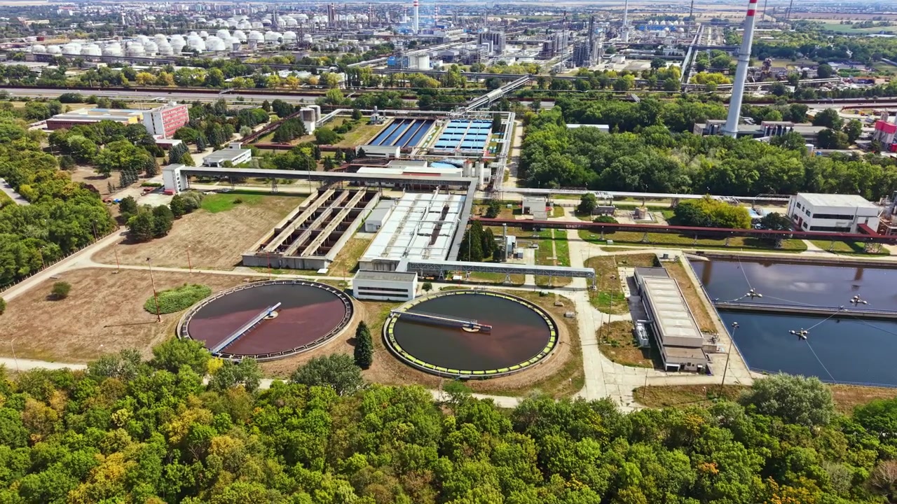 Water treatment facility with many tanks and buildings surrounded by green trees during the day