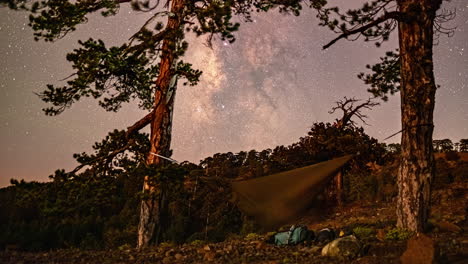 Tiro-De-Lapso-De-Tiempo-Del-Movimiento-De-Las-Estrellas-Sobre-Un-Excursionista-Durmiendo-En-Una-Hamaca-Que-Se-Balancea-Entre-Los-árboles-En-Un-Camping-Sereno-A-Lo-Largo-Del-Monte-Olympos,-Chipre-En-La-Noche