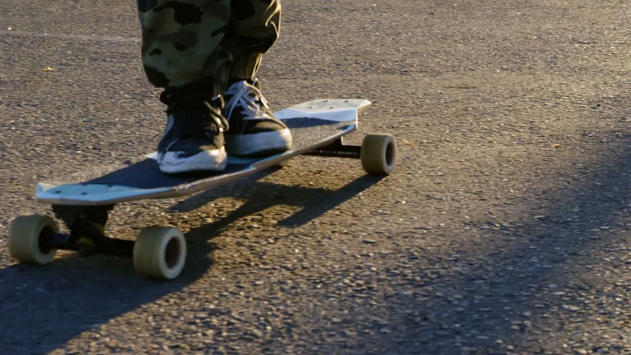 sección baja de un joven patinador montado en patineta en una carretera de campo 4k