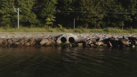 orbiting shot of drainage pipes surrounded rocks by the river