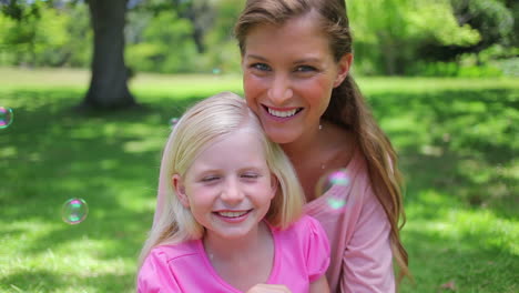 Mother-sitting-with-her-daughter-who-is-blowing-bubbles