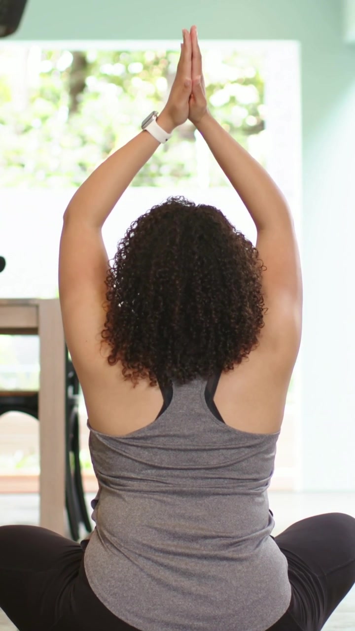 Vertical video: Lowering from overhead, woman in tank doing yoga at home on green mat with watch