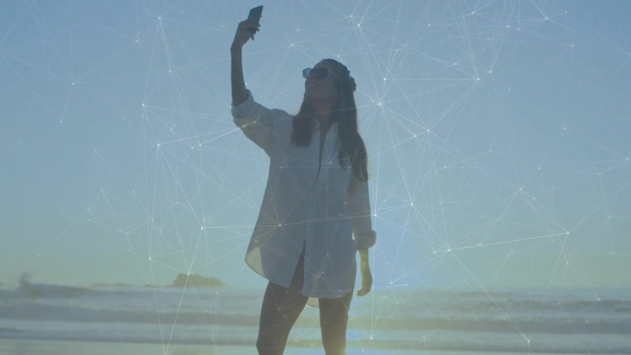 Donna che si sposta e poi alza il telefono sulla riva, riprendendo contenuti tech con effetto lens flare