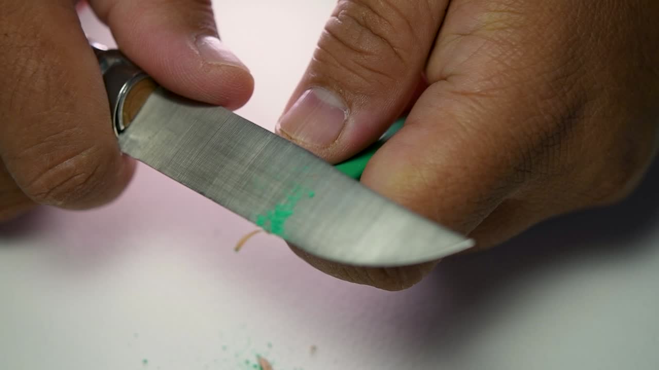 Footage of hands slowly sharpening a pencil and some coloured pencils with a sharp knife