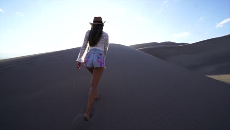 Sun-flare-cinematic-female-women-actress-model-cowgirl-outfit-slowly-walking-up-ridge-Colorado-The-Great-Sand-Dunes-National-Park-scenic-mountain-landscape-gold-hour-light-adventure-Rocky-Mountains