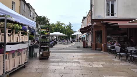 a bustling street scene in a european town, with market stalls, cafes, and people enjoying the day