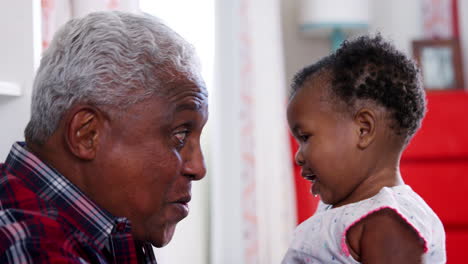 grandfather lifting baby granddaughter into the air and smiling at home