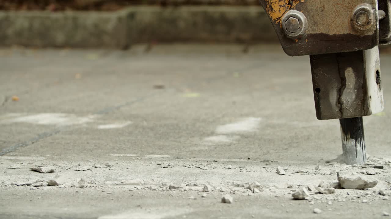 Close-up of excavator hydraulic arm rock breaker working on concrete road with sound
