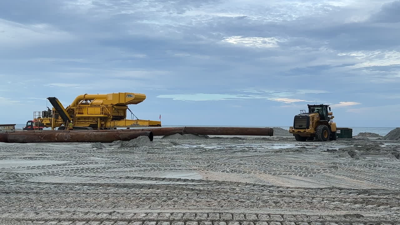 Construction workers moving pipes pumping sand from ocean,replinish