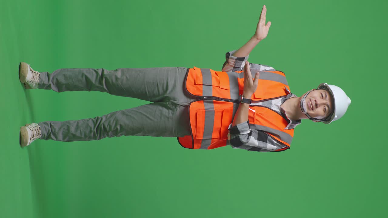 Full Body Of Asian Male Engineer With Safety Helmet Smiling And Pointing To Side While Standing In The Green Screen Background Studio