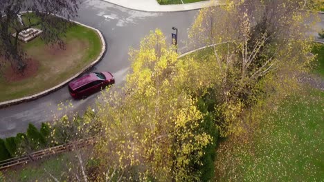 Antena-Cenital-De-árboles-Otoñales-Y-Una-Inclinación-Hacia-Arriba-Hasta-Una-Minivan-Roja-Que-Ingresa-Al-Estacionamiento-De-Una-Iglesia-En-Lafayette-Hill,-Pensilvania