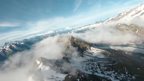 fpv drone aerial shot above clouds over steep mountain in summer, in switzerland, with partly cloudy sky and sun and cloud inversion, close to mountain glacier