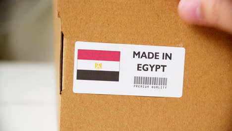 hands applying made in egypt flag label on a shipping cardboard box with products. close up shot with premium quality barcode