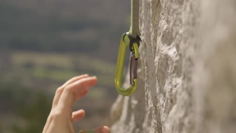 close up: unrecognizable female rock climber clips belay rope into a carabiner.