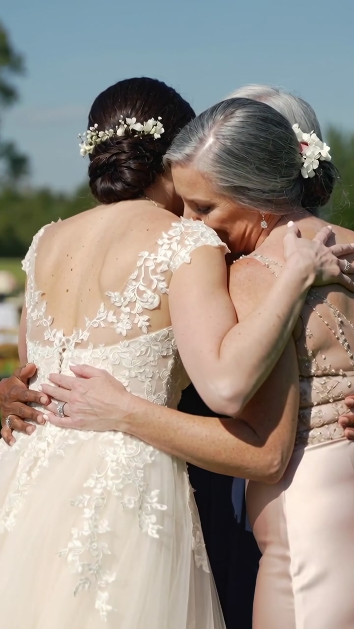 Vertical video: Turning, bride in wedding gown and two women closing, embracing for comfort on lawn