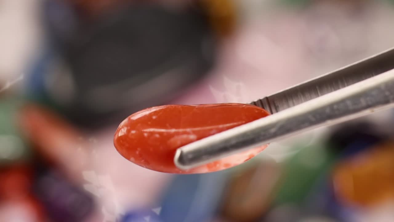Primo piano di pinzette in metallo che selezionano una pietra di diaspro rosso lucido da una vivace collezione di cristalli