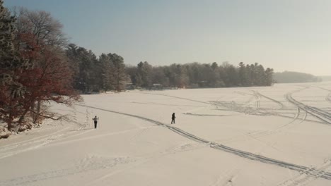 aerial of two people cross country skiing on a snow covered frozen lake during winter