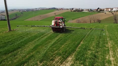 vista aérea del tractor agrícola rojo rociando en el campo con rociador, herbicidas y pesticidas insecticidas en el campo verde tierra arada, tiro medio