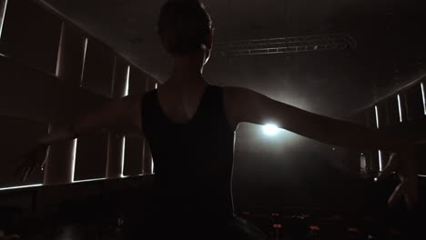 cámara lenta: el prima ballet repite una actuación en solitario de pie en el escenario del teatro en el humo en un vestido negro a la luz.
