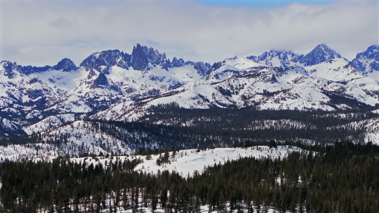 The stunning winter spring snowy jagged towering peaks of the Minarets Summit Mountains Mammoth Lakes California aerial drone sunny clouds daytime deep backcountry deep snow vista point parallax